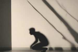 Klęczący cień mężczyzny, lekko pochylony do przodu na jasnej ścianie- ilustracja do artykułu na temat zaburzeń lękowych