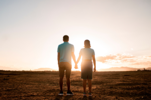 Para mężczyzna i kobieta, trzymają się za ręce na tle zachodzącego słońca. Ilustracja do artykułu o zawyżonych wymaganiach względem partnera